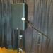 A black speaker on a stand is positioned behind a microphone on a stand, with dark curtains in the background and a wooden floor beneath.