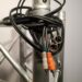 A tangled bundle of audio cables is wrapped around a metal pole. The cables include a pair of RCA connectors, one white and one orange, and two XLR connectors. The pole is part of a metallic truss structure.