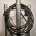 Coiled black electrical cable with connectors draped over a metallic truss against a plain background.