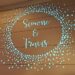 A decorative light display on a wall shows the names Simone & Travis surrounded by a circle of small blue dots.