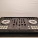 DJ mixing console with various controls, buttons, and two large jog wheels, set against a plain background. The equipment is primarily black and gray with white accents, designed for music mixing and performances.