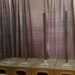 Four vertical metal poles are aligned in front of a dark, textured curtain. They are mounted on rectangular bases, evenly spaced in a row.