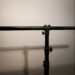 A black metal stand with adjustable clamps and a horizontal bar is set against a plain white background. Shadows of the stand are visible on the wall behind it.