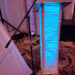 A podium wrapped in white fabric lit with blue light stands on a patterned carpet. A microphone is positioned on a stand in front of the podium, with draped white curtains and stage equipment in the background.