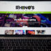 A laptop screen showcases the homepage of Rhinos Lighting and Sound. Amidst a colorful image of DJ equipment, text highlights their DJ, lighting services, and media player options, all neatly organized under the top menu. The scene is set against a dark background for added contrast.