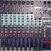 A top-down view of a DDA DM12 audio mixing console with numerous knobs, switches, sliders, and input/output ports, used for professional sound mixing and audio control.