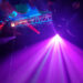 A vibrant after-grad party scene features a ceiling covered in colorful balloons, with bright purple spotlights creating beams of light. The illuminated area is bathed in a mix of pink, blue, and red hues, enhanced by an electrifying DJ package to amplify the festive atmosphere.