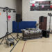 A DJ setup for an elementary school dance features speakers, lighting stands, and a table covered by a Rhinos banner. Pink balloons, a blue mat, and colorful wall decorations set the perfect scene for a fun school dance DJ package.