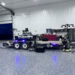 A mobile DJ setup on a trailer with Rhinos written on the side, flanked by speakers and lights inside a spacious garage. Gold and black balloons say Congrats Grad. Equipment and shelves are visible in the background.