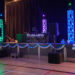A decorated stage in a gym with colorful lights, blue and white balloons, and garlands. A DJ booth labeled Rhinos is centered, with speakers and equipment on either side. Twinkling string lights frame the scene.