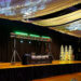 A decorated event stage with DJ equipment, a table labeled “Rhino’s,” green stage lights, illuminated white trees, and draped white fabric with string lights hanging overhead.